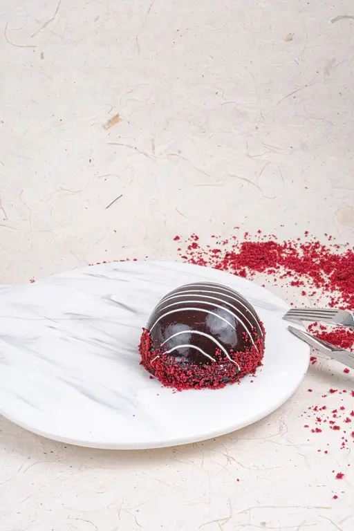 Glazed chocolate dome mono cake with white drizzle on a cherry base.